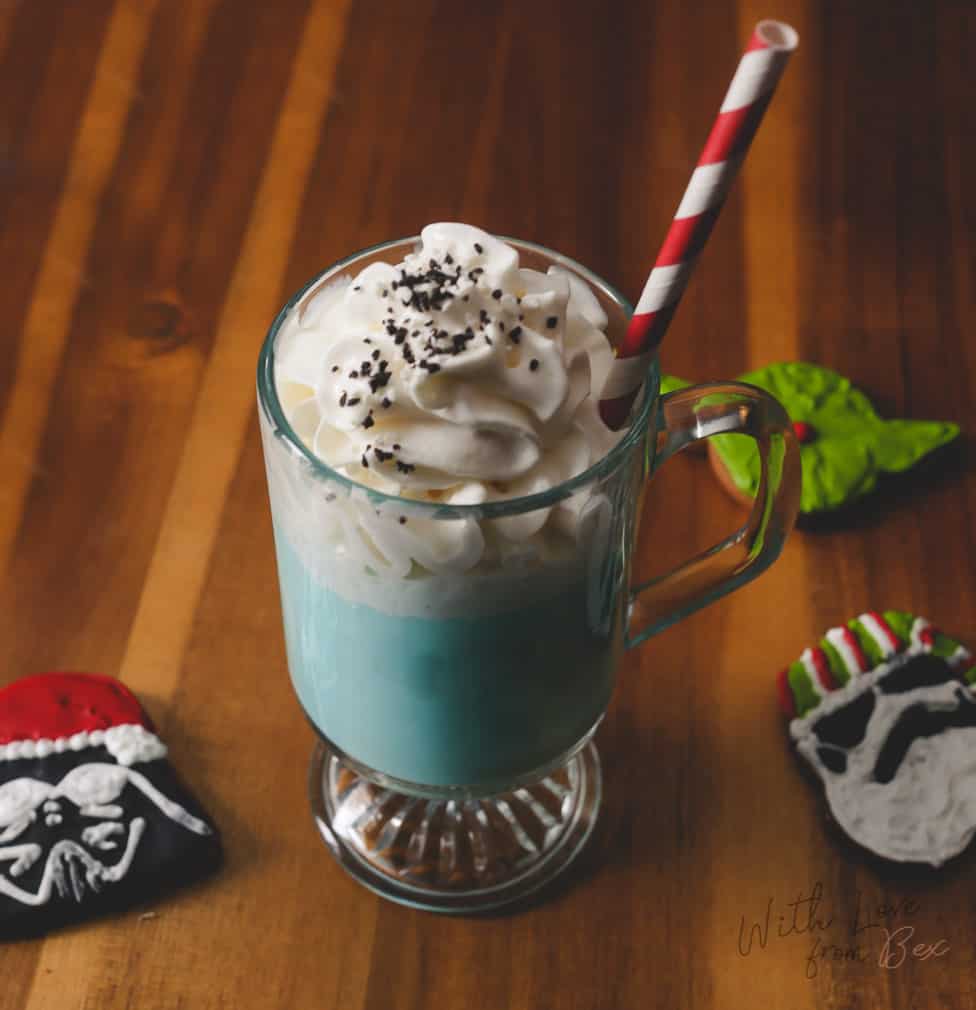 a tall clear glass with blue milk hot chocolate surrounded by christmas star wars cookies